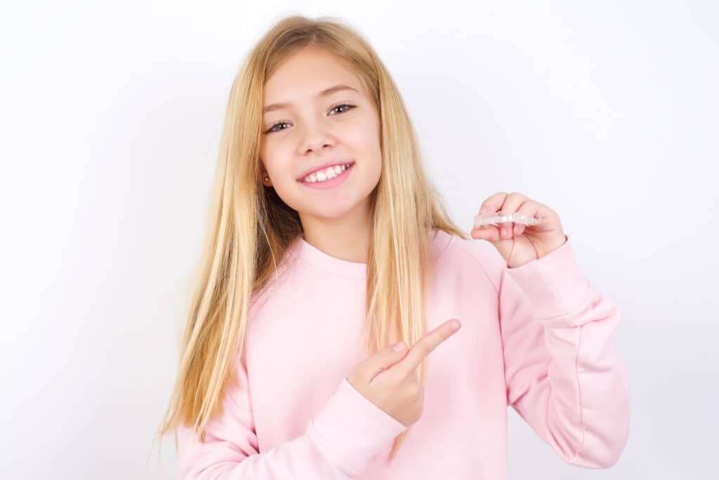Young girl smiling and pointing at her new Invisalign aligners, ready to start her treatment
