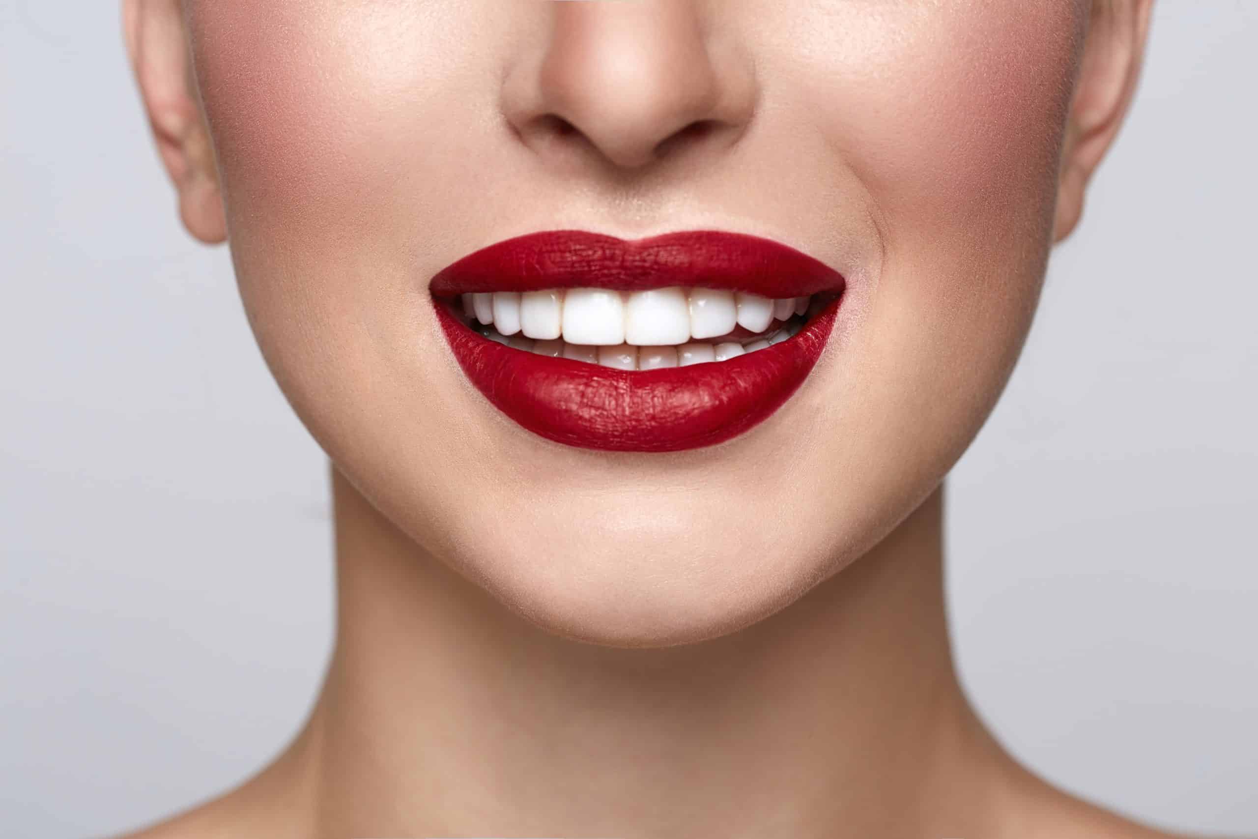 Lower half of a woman's smiling face with white teeth and red lipstick