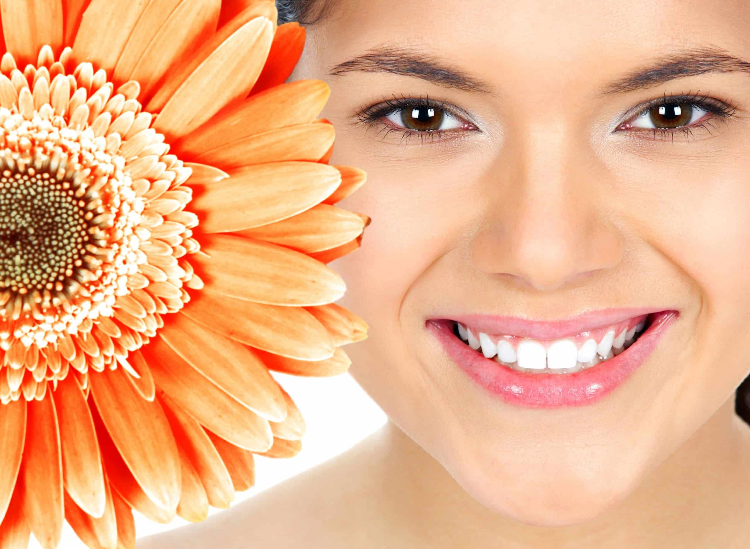 Woman smiling next to a giant orange flower on a white background