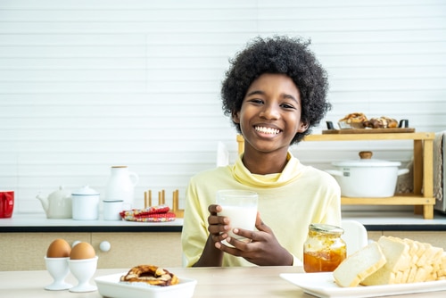 African-American boy drinking milk and eating bread with egg.