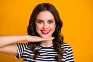 Woman smiling brightly with a hand touching her face to highlight her shiny, white veneers