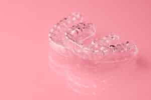 A set of clear dental retainers on a pink background, necessary for long-term smile care