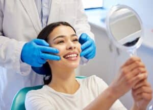 Woman smiling while looking in the mirror at her new veneers at the dental office