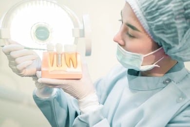 Dentist holding a model of multiple teeth, one with a dental implant.