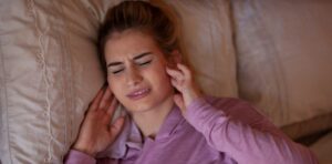 Woman having trouble sleeping and clutching her jaw in pain from TMJ disorder, in need of dental treatment.